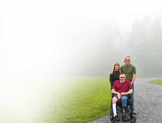 Wounded warrior Jason Ehrhart sitting on a wheelchair with his parents and caregivers Pam and Mike Estes.