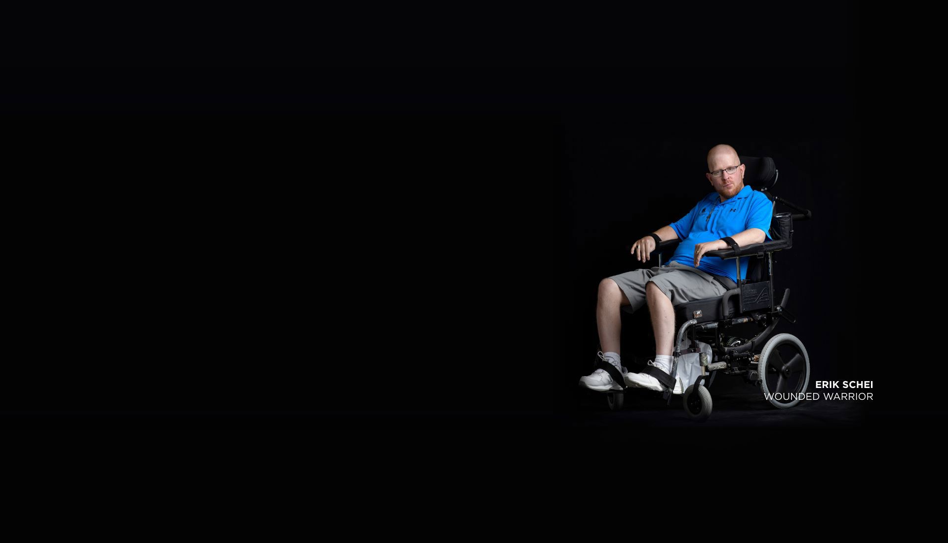 Wounded warrior Erik Schei looking directly into camera with serious expression. He’s in a wheelchair on a black background.