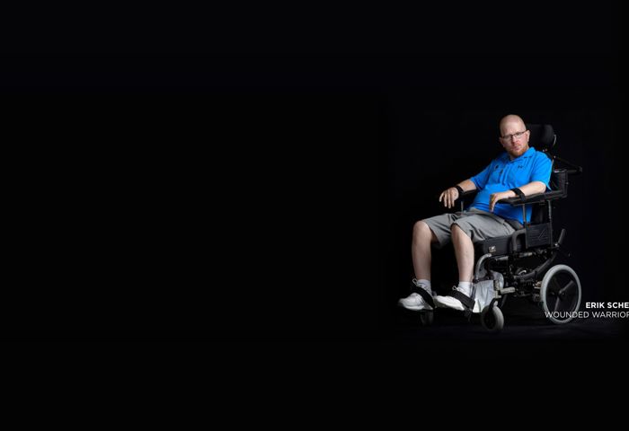 Wounded warrior Erik Schei looking directly into camera with serious expression. He’s in a wheelchair on a black background.