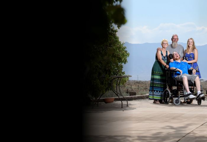 Wounded warrior Erik Schei with his parents and sister smiling in front of mountains. Erik is in a wheelchair.