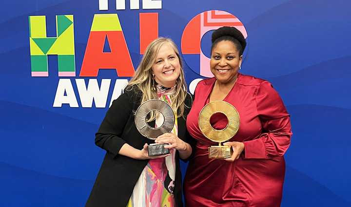 A female WWP employee holding a silver trophy stands smiling next to a female CSX executive holding a gold trophy in front of a sign that says Halo Awards.