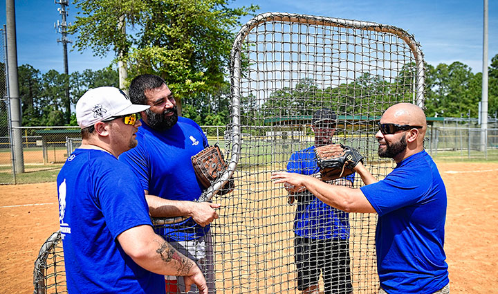 Wounded warrior Carlos De Leon stands on a baseball field with three fellow warriors.