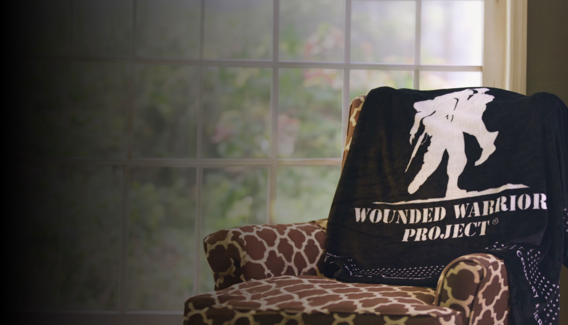 A black fleece blanket featuring the Wounded Warrior Project® logo with a border of small stars is draped on an armchair.