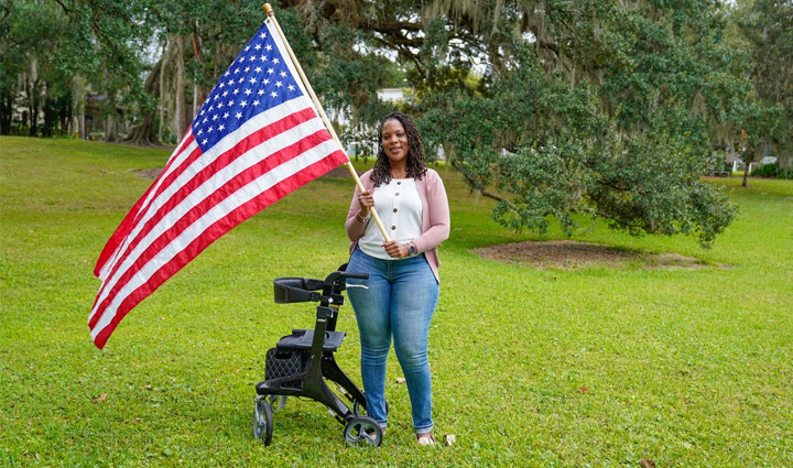 WWP warrior Sharona Young stands outside holding an American flag with her walker by her side.