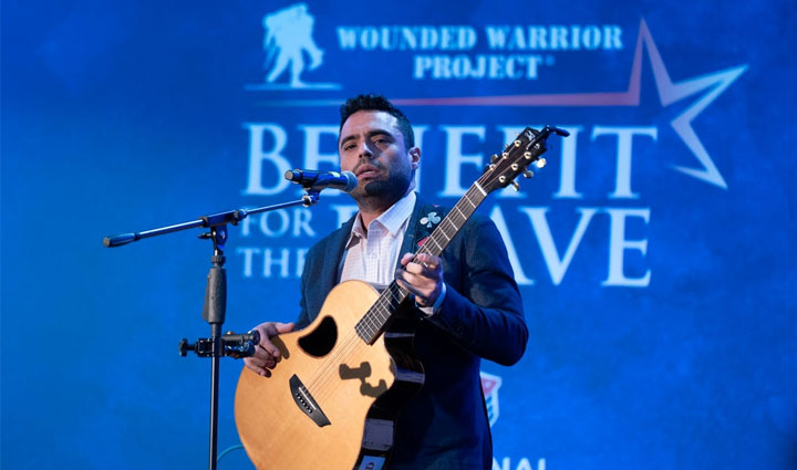 El veterano herido Sal Gonzales tocando su guitarra mientras canta con un micrófono en un evento Benefit for the Brave.