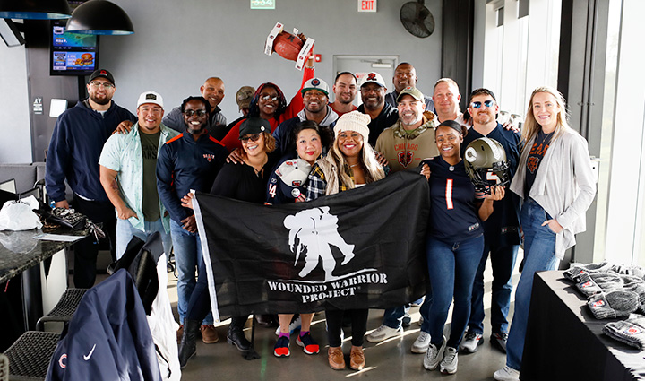 A group of male and female warriors holding a WWP flag and several former Chicago Bears players stand together during a connection event at Top Golf.