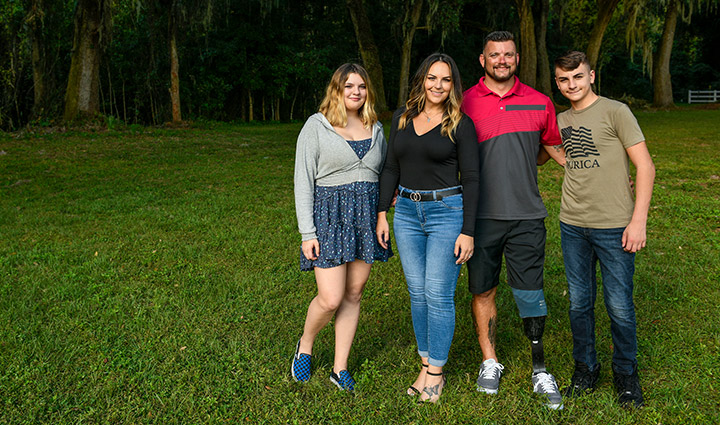 Wounded warrior Sean Karpf stands outside near trees with his wife, and teen-aged daughter and son.