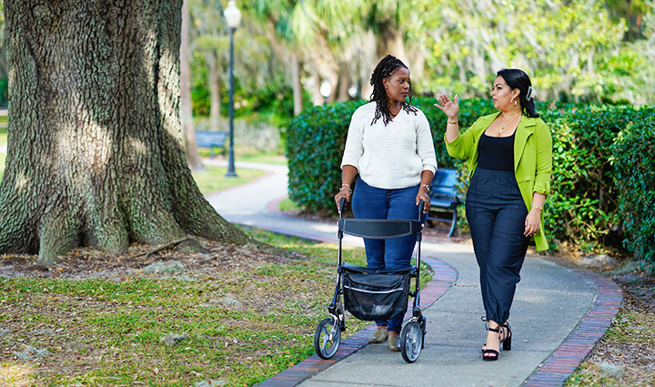 Wounded warriors Sharona Young and Yomari Cruz walking in a park. Sharona uses a walker for support as Yomari gestures while they talk.