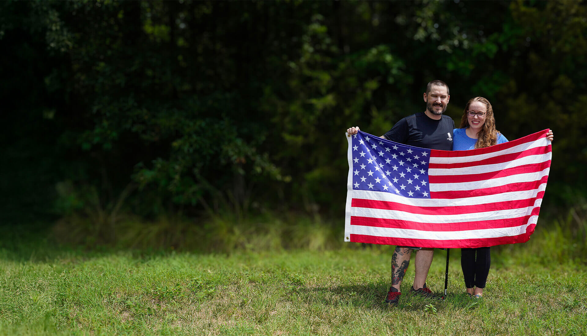 Wounded warrior Xander Hernandez and his wife, Jessica, stand outside while holding up an American flag.