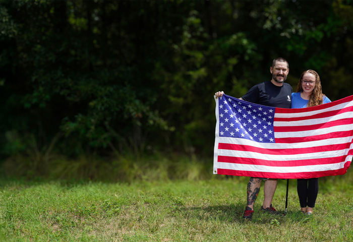 Wounded warrior Xander Hernandez and his wife, Jessica, stand outside while holding up an American flag.