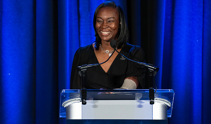 Wounded warrior Danielle Green stands at a podium with a microphone while smiling.  