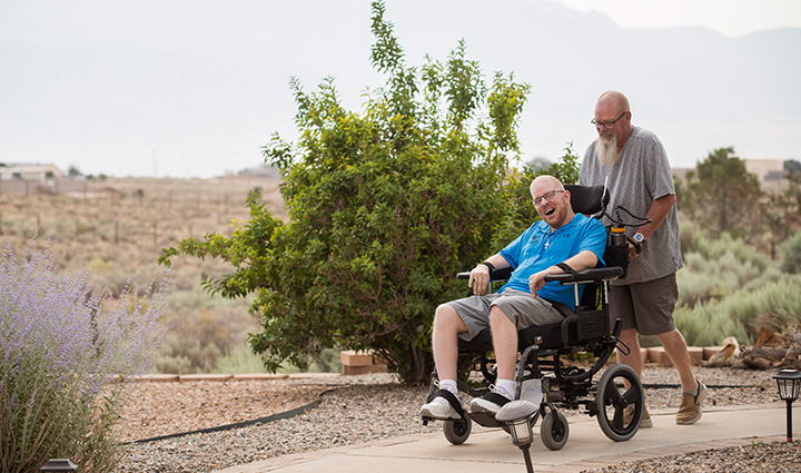 Wounded warrior Erik Shei laughing while being pushed in a wheelchair by his father outdoors on a fall day.