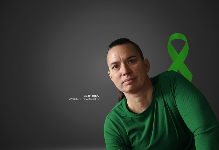 Wounded warrior Beth King in a green shirt sits against a gray background with a green Brain Injury Awareness ribbon.