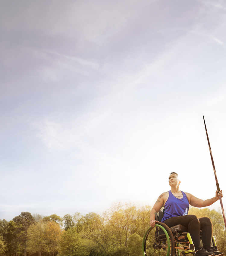 La veterana herida Beth King sentada en una silla de ruedas y sosteniendo una jabalina en un campo de atletismo.