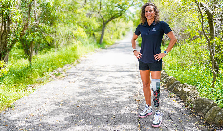 Wounded warrior Kelly Elminger stands confidently on a lush outdoor path, showcasing her prosthetic leg's vibrant design.